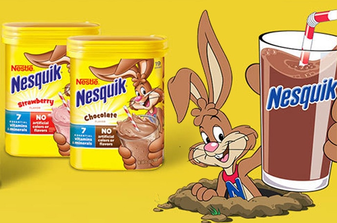 The NESQUIK Bunny pops out of a hole with a glass of chocolate milk beside two containers of NESQUIK powder.