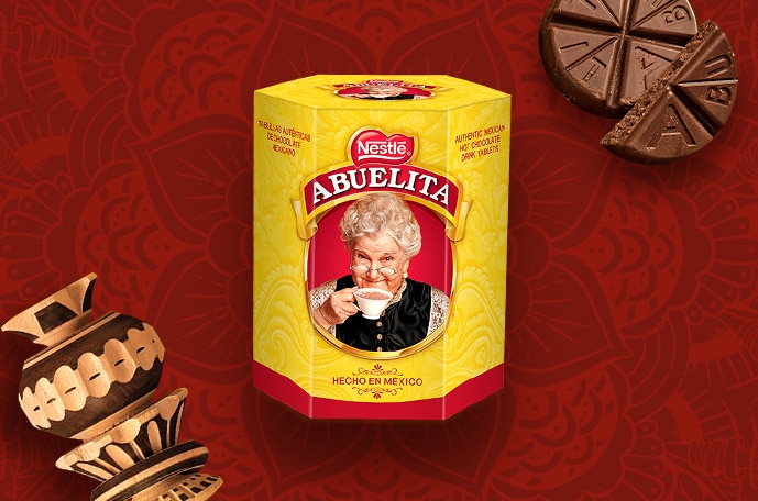 Packaging of ABUELITA tablets beside tablets and a molinillo on a red background with mandalas.