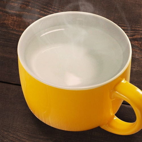 Una taza color amarillo con humeante agua caliente sobre una mesa de madera. Una taza color amarillo con humeante agua caliente sobre una mesa de madera.