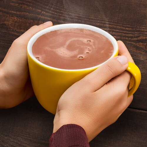Manos sostienen una taza amarilla con humeante chocolate caliente sobre una mesa de madera. Manos sostienen una taza amarilla con humeante chocolate caliente sobre una mesa de madera.