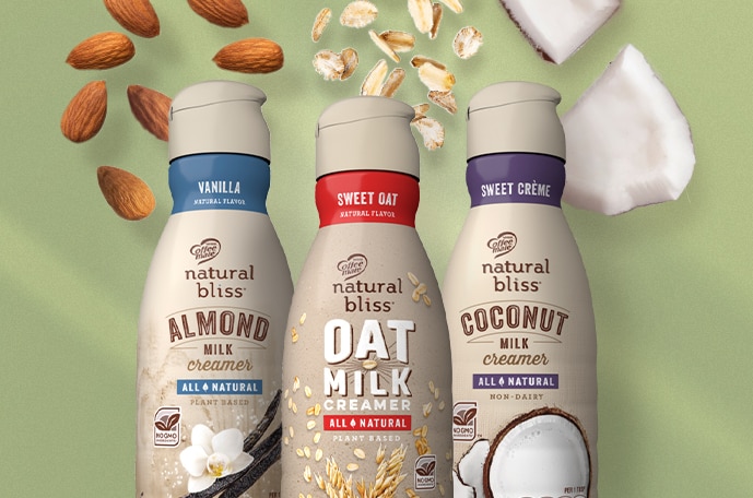 Tres botellas de creamer y avena, almendras y coco cayendo detrás.