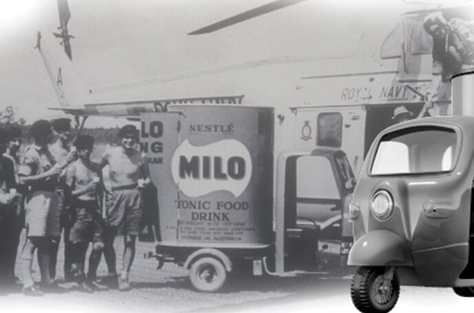 Una imagen en blanco y negro de un antiguo scooter y un grupo de personas de pie cerca de un camión de reparto de MILO.