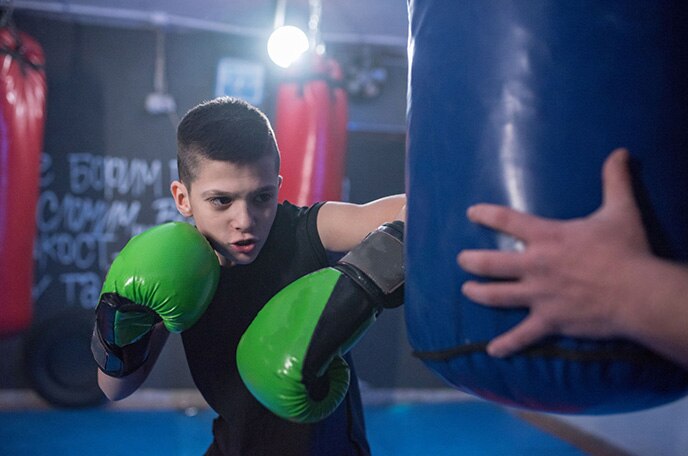 El logotipo de ACTIV-GO® sobre una imagen de un chico con guantes de boxeo verdes golpeando un saco de boxeo.