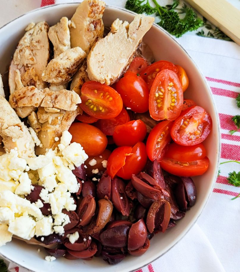 A bowl of chicken, feta cheese, kalamata olives and cherry tomatoes.