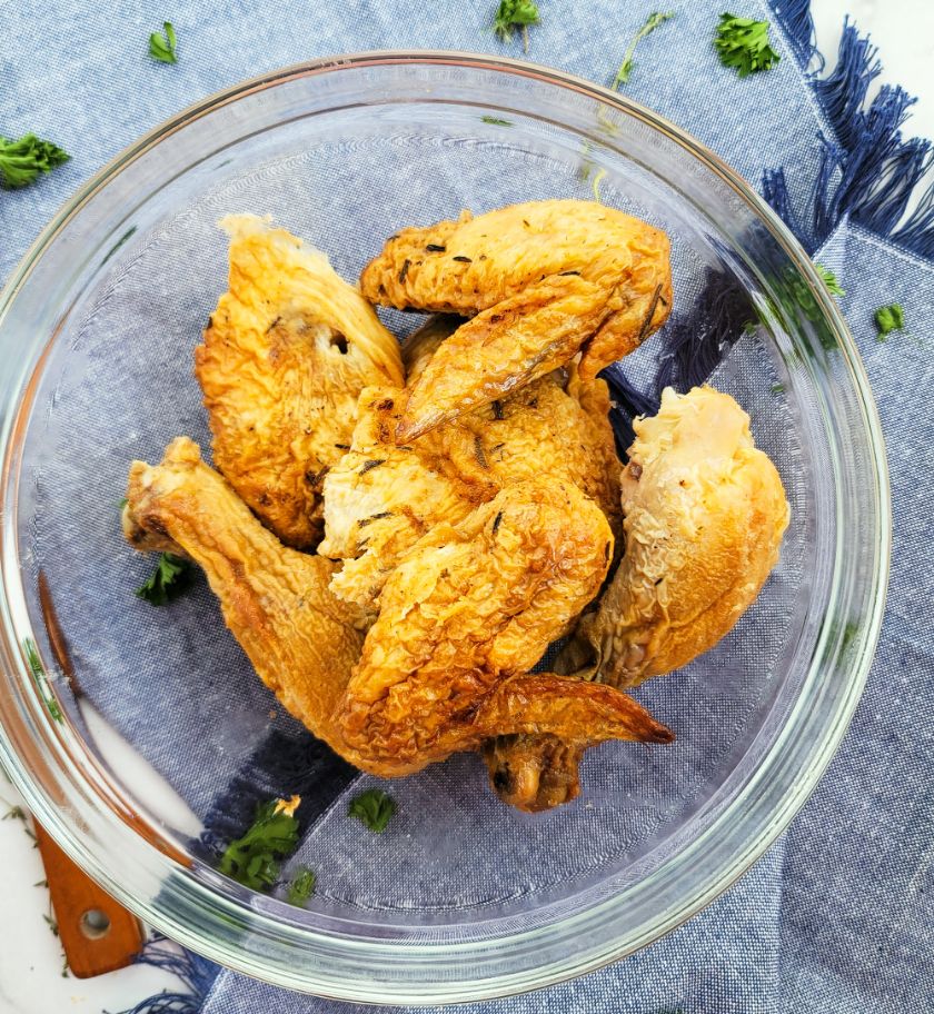 Un tazón de sobras de pollo sobre una servilleta de tela con hierbas de olor esparcidas.