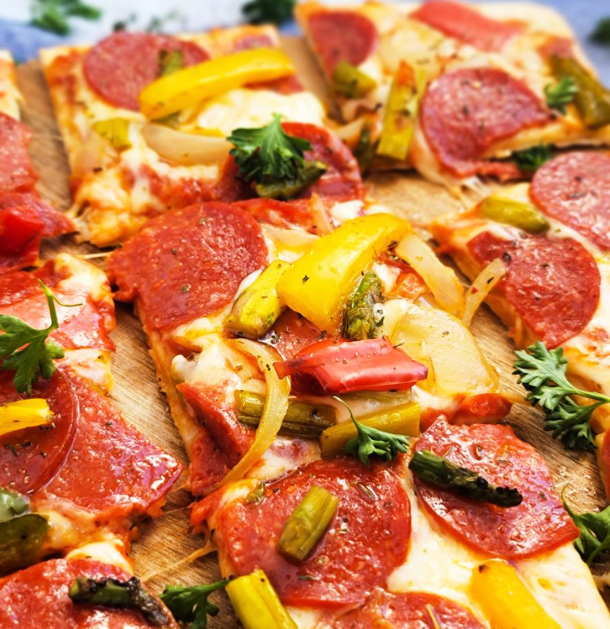 Una pizza DiGiorno de pepperoni masa delgada cubierta de pimientos, cebolla y espárragos cortados en cubos sobre una pala de madera.
