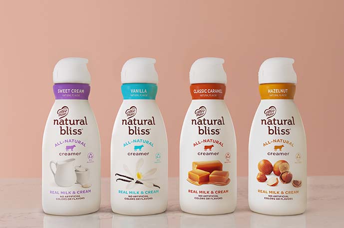 Bottles of Sweet Cream, Vanilla, Classic Caramel and Hazelnut natural bliss creamers lined up against a pink background.