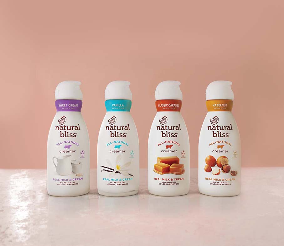 Bottles of Sweet Cream, Vanilla, Classic Caramel and Hazelnut natural bliss creamers lined up against a pink background.