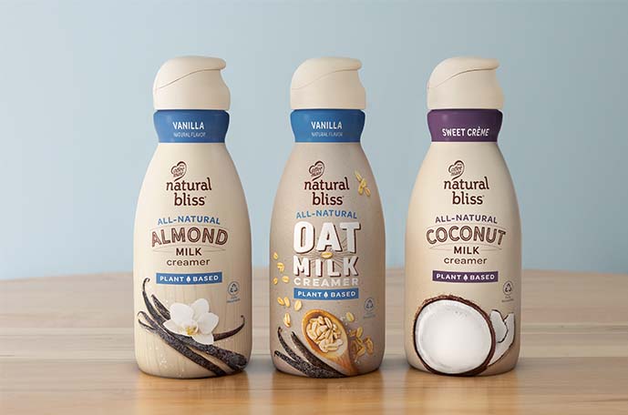 ottles of Vanilla, Vanilla Oat Milk and Sweet Créme natural bliss creamers lined up against a blue background.