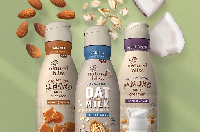 Three bottles of natural bliss creamer with oats, almonds and coconut falling behind them.