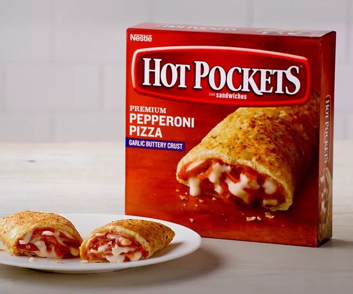 Pepperoni Pizza Hot Pockets cut in half sits in front of the box against a white surface and white tiled backsplash.