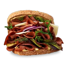 Layers of Plant-Based Ham Slices between red onions, sprouts, pickles, and Swiss cheese, on wheat bread.