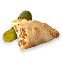 A whole dill pickle besides a Cubano Empanada with a bite missing to reveal ham, olives, cheese, and pickles.