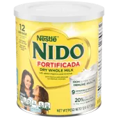 Una lata de Nido Fortificada con una etiqueta amarilla, una tapa blanca y un corazón dorado sobre un vaso de leche vertida.