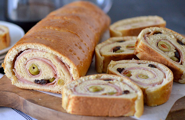 A loaf of Venezuelan ham bread beside slices stuffed with ham and green olives.