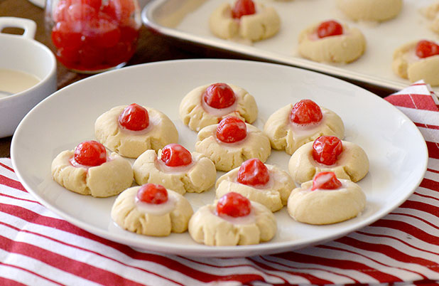 A plate of almond shortbread cookies topped with cherries and icing.