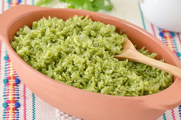 Un plato de barro servido con arroz verde sobre un colorido mantel.