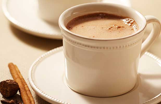A white mug of ABUELITA on a white saucer beside cinnamon sticks.