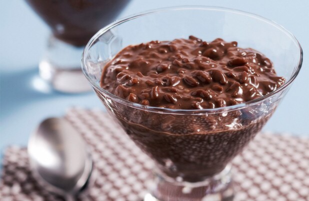 A clear dish of chocolate rice pudding beside a spoon.