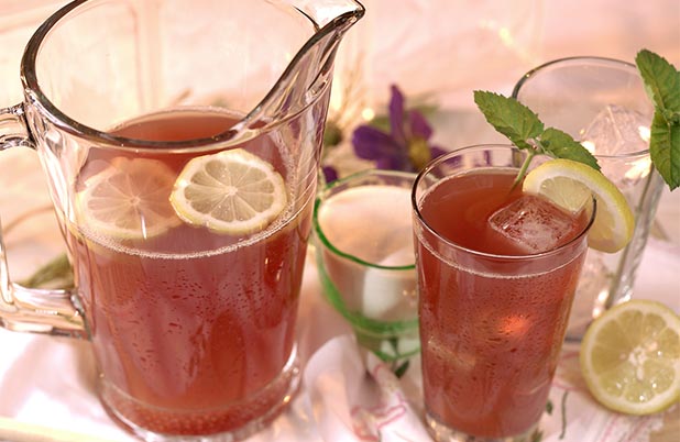 A pitcher and glass filled with berry lemonade, ice, lemon slices and mint garnish. 