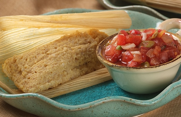 Un tamal de quinoa abierto sobre un plato de cerámica azul junto a un tazón de salsa.