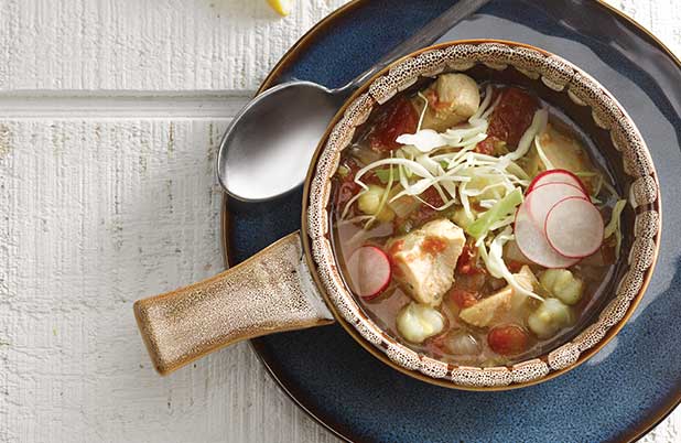 A ceramic bowl of chicken posole with cabbage and radish.