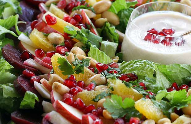 A Christmas eve salad filled with pomegranate seeds and apple slices around a cup of dressing.
