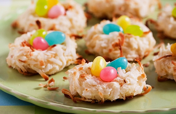 Coconut macaroons topped with candy eggs on a green plate.