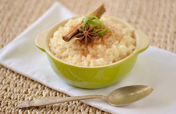 A green dish filled with Cuban rice pudding topped with lime rind, anise and cinnamon sticks.