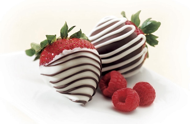 White and dark chocolate dipped strawberries on a cloth napkin with fresh raspberries.