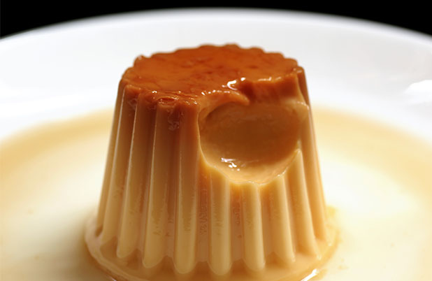 A small flan on a white plate with a bite taken from it.