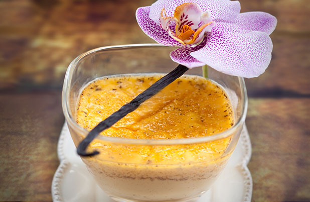 A clear dish filled with vanilla bean flan with a vanilla bean garnish.