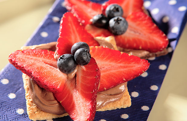 Graham crackers topped with chocolate and fresh strawberries and blueberries on a cloth napkin.