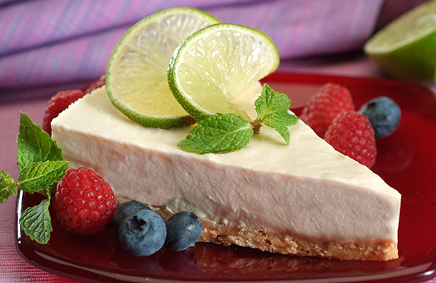 A slice of lime pie with lime and mint garnish on a plate with fresh berries.