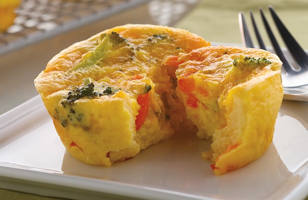 A mini quiche with broccoli and cheddar cut open on a plate with a fork.