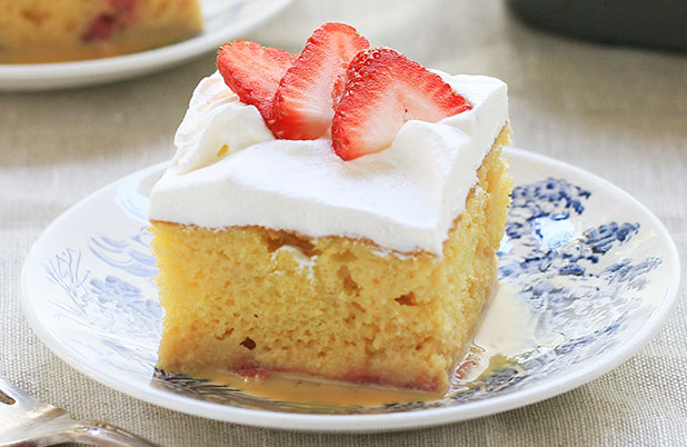A square slice of tres leches cake topped with strawberries.