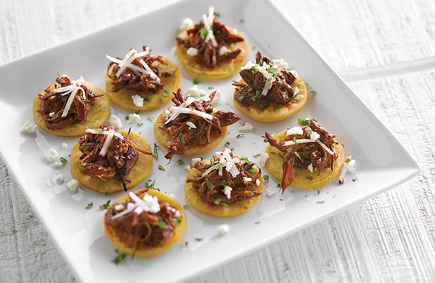 A plate of tamale tartlets made of corn masa topped with pork, cilantro and cheese.