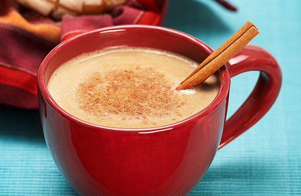 A red mug filled with hot chocolate and a cinnamon stick on a white table cloth.