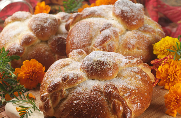 Three loaves of Pan de Muerto dusted with sugar and surrounded by flowers.