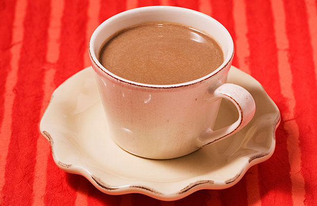 A white mug filled with chocolate pumpkin atole on an orange table cloth.