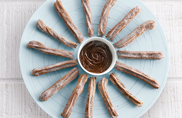 A cup of ABUELITA dipping sauce surrounded by churros on a plate.