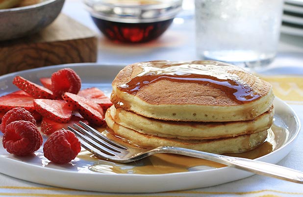 Una pila de panqueques con sirope sobre un plato con un tenedor, fresas y frambuesas.