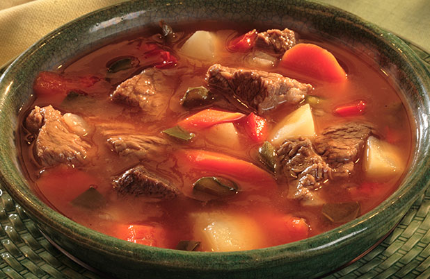 A green ceramic bowl full of beef stew and vegetables.