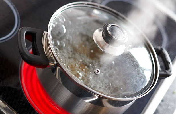 Water boils in a pot with a lid and steam rises from it.