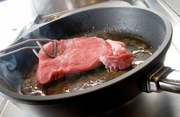 A piece of steak is seared in a skillet.