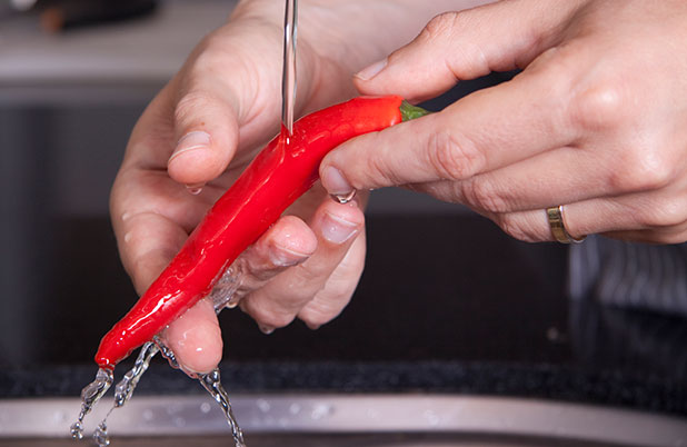 Hands rinse a red chili pepper.