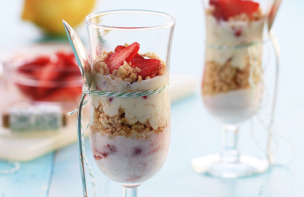 A champagne flute with a spoon tied around it filled with strawberry granola yogurt parfait.