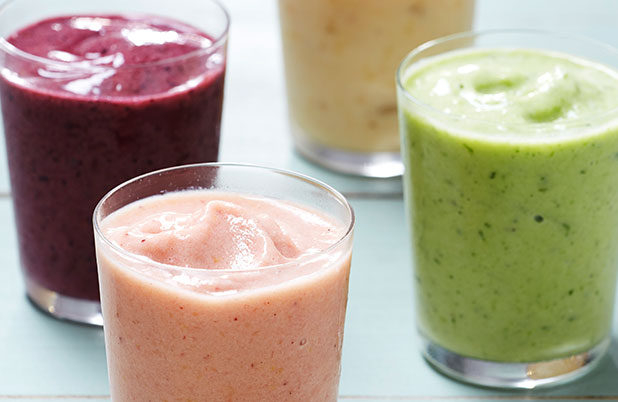Purple, green, pink and yellow fruit smoothies in glasses on a blue table.