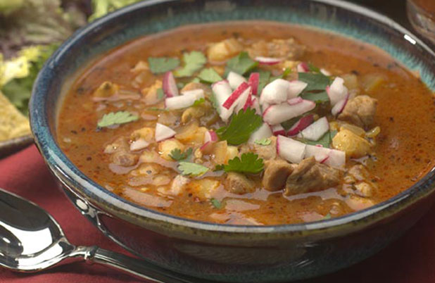 A ceramic bowl of stew garnished with radish and cilantro.