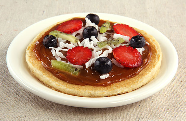 A fruit pizza made with a pancake, chocolate spread, fresh fruit and shredded coconut.